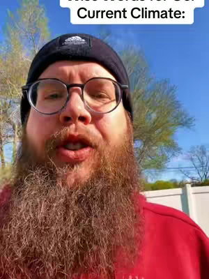 A man with a full beard wearing glasses and a black beanie is centered in the frame, with text overlays in the top portion of the image. The background includes a bright blue sky and hints of green foliage, suggesting an outdoor setting.