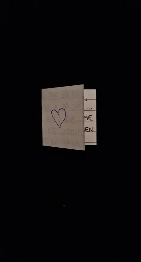 The cover image shows a folded note or card against a black background. The card is partially opened, revealing text and a drawn purple heart. The overall composition is minimalist.