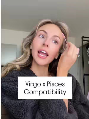 A woman with long blonde hair is applying makeup with an eyebrow brush. A white rectangular text overlay displays the words "Virgo x Pisces Compatibility". The background is a room lit with natural light.