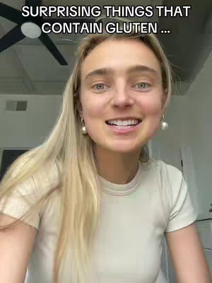 A woman with long blonde hair and pearl earrings smiles at the camera. Above her head, text overlayed reads, "SURPRISING THINGS THAT CONTAIN GLUTEN ...". The background is a room with a ceiling fan.