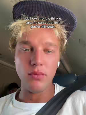 A young man in a light-colored shirt and a blue hat is centered in a selfie-style shot, with text overlayed. The background suggests an interior, possibly a vehicle. The man's expression appears focused.