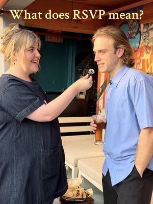 A woman in a dark denim dress is holding a microphone and interviewing a man in a blue shirt. Above them, text reads "What does RSVP mean?". They are outside, there is a blurred background with graffiti and a bar.