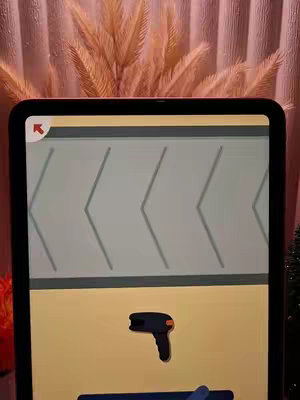 The cover image shows a digital screen, likely an iPad, displaying a game interface. In the background, out-of-focus, are dry, feathery plants behind the iPad. The screen displays a puzzle game. The color palette is warm, with beige, yellow, and orange tones.