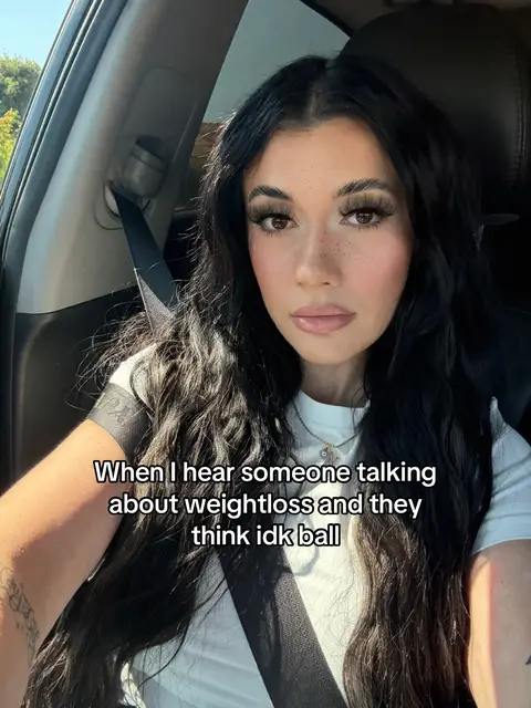 The image shows a woman in a car, looking straight at the camera with a thoughtful expression. She has long, dark hair and is wearing a white shirt. There is text overlayed on the bottom of the image.