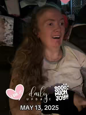 The cover image features a woman with long, wavy blonde hair, smiling and looking upward with an open mouth, likely in mid-conversation. Overlayed on the image are several text elements and stickers, including "Love It" in a heart-shaped sticker, "daily update" in stylized text, and the date "MAY 13, 2025" at the bottom. Additional text says "sooo MUCH JOY!!" in a cartoonish style. The overall composition suggests a positive, upbeat video.