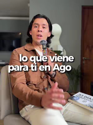 A man in a brown jacket holds a microphone and speaks, with white text overlaying the image. He's seated with a book in the background, suggesting a setting for a motivational video, with a soft lighting.