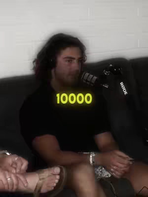 A man with long hair is seated in front of a microphone, wearing a black shirt. The text "10000" is overlaid in a yellow font. The overall composition suggests a podcast or interview setting.