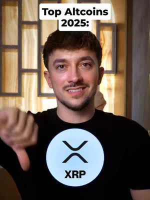 A man with short brown hair and a mustache is shown in a medium shot, his expression slightly downward, wearing a black t-shirt. The shirt features a circular design with the XRP logo at the center.