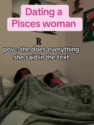 The image shows a bedroom scene with two people lying under a blanket. Text overlays are present, including a light pink rectangular banner reading 'Dating a Pisces woman,' sitting above the text 'R', and a caption that says 'pov: she does everything she said in the text.' The setting appears to be a neutral-toned room, and the composition is dimly lit.