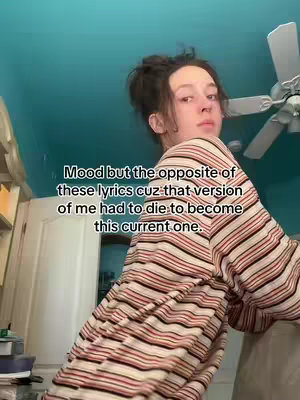 A young woman in a striped long-sleeved shirt looks back at the camera near a fan. A text overlay is visible on the left.
