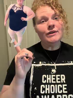 A person is holding up one finger, upon which a cartoon cutout of a person is standing. The person in the foreground is wearing a black shirt with the words "Cheer Choice Awards" on it. To their left, there's a cartoon cutout of a woman in a black swimsuit.