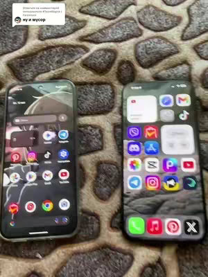 The image shows two smartphones side-by-side, each displaying their home screens. The phone on the left appears to be an Android device, with a darker theme and a variety of app icons arranged in a grid. The phone on the right is an iPhone, showcasing a lighter, more minimalist aesthetic. Both phones are placed on a patterned, brownish surface.