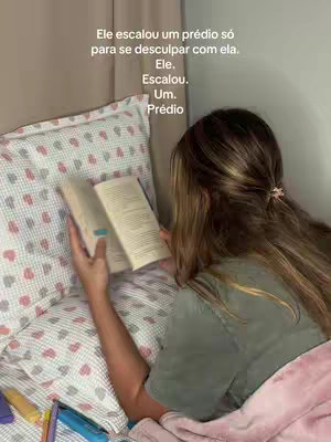 A woman with long brown hair is reading a book while lying in bed. The image is composed with soft lighting and muted colors, creating a cozy and intimate atmosphere. The woman is partially covered by a pink blanket.