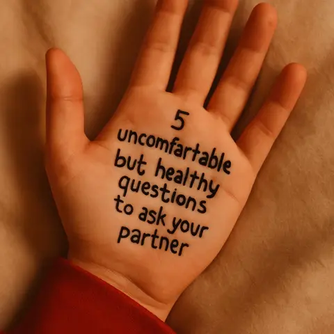 A hand is shown, palm up, against a light tan background that appears to be fabric. Handwritten text is written on the palm in black ink, which reads: "5 uncomfortable but healthy questions to ask your partner."