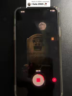 The image shows a phone displaying an image. The phone screen is mostly dark, with a full moon visible in the background. A tombstone with a Lego minifigure on it and some text is in the middle of the screen. Overlayed on the screen are the recording controls.