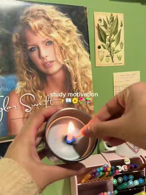 The image shows a person lighting a candle with a match. Behind the candle is a poster of Taylor Swift. A piece of artwork hangs on the top right.