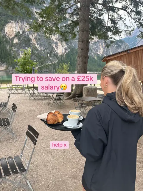 A person holding a tray with coffee and croissants in a cafe next to a lake and mountains. The person is seen from the back.