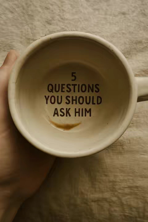 An overhead shot captures the interior of a beige coffee mug, with a small patch of residual coffee at the bottom. Stenciled in bold, dark text within the mug is the phrase "5 QUESTIONS YOU SHOULD ASK HIM."