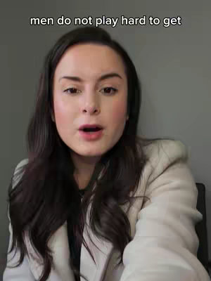 A woman with long, dark hair is centered in the frame, looking directly at the camera. She wears a light-colored blazer over a dark top. The background is a plain, neutral gray. The text overlay reads 'men do not play hard to get'.