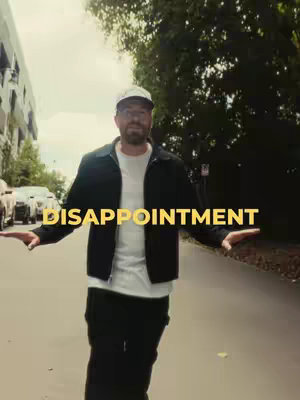 A man wearing a baseball cap and a black jacket stands outdoors with his arms outstretched, the word "DISAPPOINTMENT" is superimposed in yellow over the image.