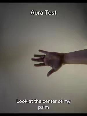 The image shows a hand with the palm facing towards the viewer against a plain background. The fingers are slightly curved. Above the hand, a text overlay reads "Aura Test" and beneath it, text reads "Look at the center of my palm".