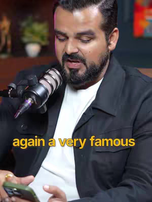 A man in a black jacket speaks into a microphone while holding a phone. A text overlay reads "again a very famous".