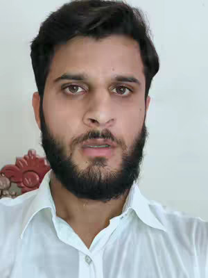 A medium shot of a man with dark hair and a beard, wearing a white collared shirt. He is centered in the frame against a plain white background. The lighting is soft and even, highlighting his face. The composition is simple and focuses on the man's expression.