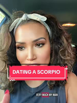 A woman with long, wavy brown hair and makeup is looking towards the front, partially obstructing the view of a car interior in the background. Overlaid on her is a rectangular text box that reads, 'DATING A SCORPIO'.