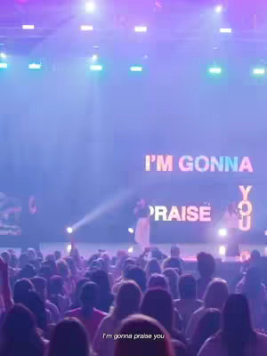The cover image is a live performance on a stage. It features a crowd of people facing the stage, where a performer is singing into a microphone. Above the performers, there's a screen displaying the text "I'M GONNA PRAISE YOU." The lighting is vibrant with purples and blues, illuminating the stage and performers.