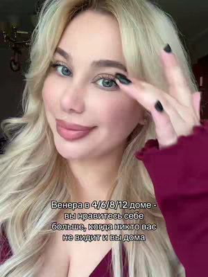 A blonde woman with blue eyes poses, holding her hand near her face with dark painted nails. Text appears on the lower part of the image.