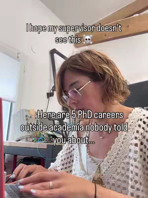 A woman sits at a desk with a laptop, the image is a selfie-style video. On the top, overlaid white text says, "I hope my supervisor doesn't see this" along with a skull emoji, showing the video creator is being discreet and maybe doing something they don't want their supervisor to see. Beneath that, centered, text reads "Here are 5 PhD careers outside academia nobody told you about...", setting the video's educational theme. The creator, a woman with short, highlighted hair and glasses, is focused on the laptop, suggesting content related to career options and job search advice.