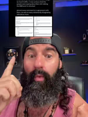 A man with a long, dark beard, mustache, and long curly hair is the primary focus. He wears a black baseball cap and a pink tank top, with a beaded necklace around his neck. He points with his right index finger towards a screen displaying a set of four screenshots of text, and he has an open mouth. The background is dark, with subtle indications of a room. The lighting appears to be overhead and slightly to the left. There are visible items on the background like a piece of art. The overall impression is one of engagement and imparting.
