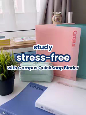 The image showcases a collection of school binders and a pencil case resting on a white table. Several brightly colored binders (pink, teal, and blue) are arranged behind and in front of the pencil case and binders. The text overlayed on the scene reads "study stress-free" in a bold, rounded font with "Campus QuickSnap Binder" beneath it. The composition is well-lit, giving the scene a clean and organized appeal, suitable for the theme of study and organization.