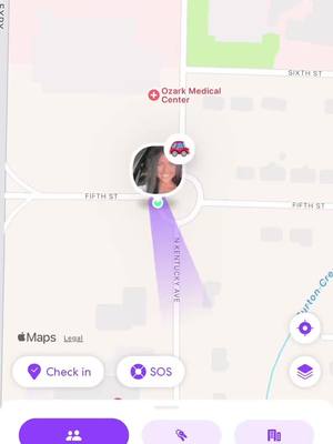The image is a screenshot from the Life360 app, displaying a map view. The central focus is a woman's face within a circular profile icon, positioned at a roundabout intersection indicated by purple directional indicators. A car icon signifies the user's location. The map features street names, a medical center marker and white and light background.