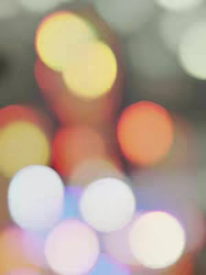 An abstract image with out-of-focus bright lights. The lights create blurred circles of various colors, including yellow, orange, and white, set against a gray background.