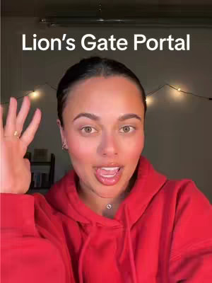 A woman with dark hair in a red hoodie faces the camera, sticking her tongue out. Above her head, text reads 'Lion's Gate Portal'. Fairy lights are visible in the background.