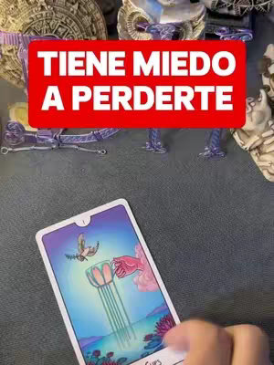 The image shows the top of a table with various objects, including a tarot card facing upwards. A rectangular red and white text overlay reads 'TIENE MIEDO A PERDERTE'. The tarot card features an illustration of a cup with a flowing stream, a floral design, and a flying bird.