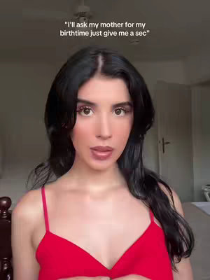 A selfie-style shot featuring a woman with long, dark hair and makeup, wearing a red top. The background is softly blurred, with text overlaid at the top. The lighting appears natural, emphasizing the woman's features and attire.