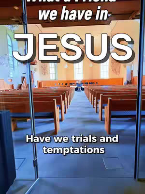 A photo taken from inside a church. The foreground shows a glass barrier with metallic supports. Inside, long rows of wooden benches face towards the altar, which is at the end of a long aisle. The walls are beige with brown accents. The lighting is bright, creating a sense of openness.
