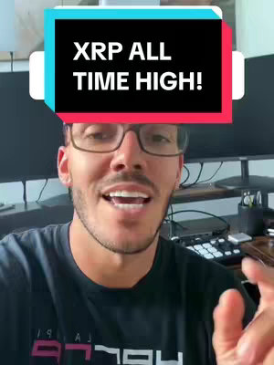 A man wearing glasses smiles while pointing, overlaid with a text box that reads "XRP ALL TIME HIGH!" in a stylized font. The background is blurred but appears to be a home office setting with monitors. He wears a black t-shirt.