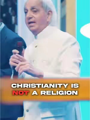 An elderly man in a white suit and holding a microphone, is standing in front of what seems to be a stage. Text overlayed announces "Christianity is NOT a religion"