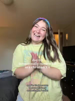 A young woman with long brown hair and a colorful headband smiles and claps her hands in front of her chest. She is wearing a yellow t-shirt. Text overlays in the image.
