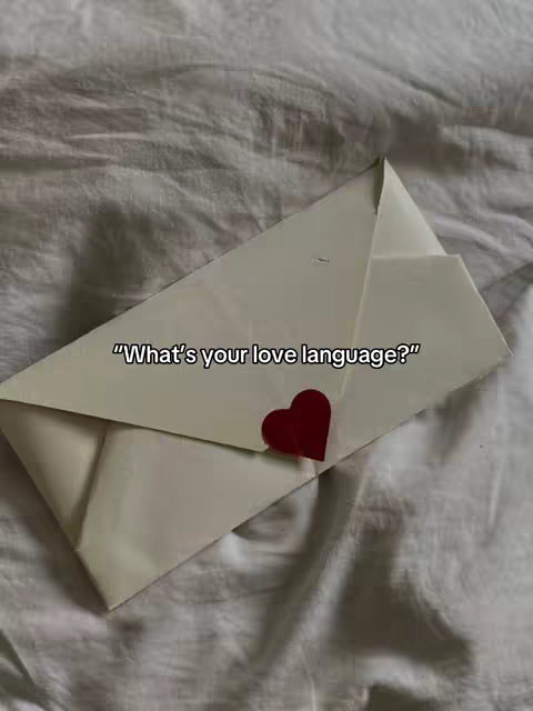 An image shows a white envelope, sealed with a red heart sticker, resting against a rumpled white surface, likely a bed sheet. Text overlayed on the envelope reads, "What's your love language?"