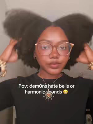 A woman with dark, curly hair and glasses is shown from the chest up.  She is looking at the camera with a slight smile and moving her hair.  There is text on the image.