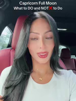 A woman with long dark hair and a white top is sitting in a car. Text overlays at the top of the image read "Capricorn Full Moon What to DO and NOT to Do". The woman is speaking with a subtle expression. The background of the car is visible, showing the seat and interior.