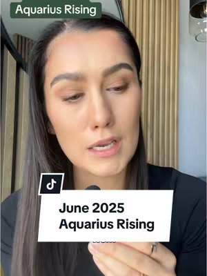 A woman with dark hair and light makeup is shown from the chest up, speaking towards the camera. A sign with text overlaid stating 'June 2025 Aquarius Rising' covers the lower portion of the image. The background is simple with blurred vertical lines, with a black microphone visible on the bottom right of the image. The woman is wearing a black top, and a part of the background are wooden elements.