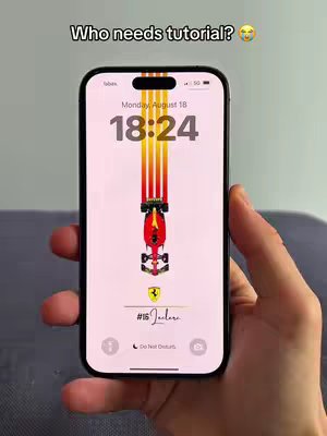 A person's hand holding a black iPhone displaying a custom Formula 1 wallpaper featuring a racing car and vertical stripes in red and yellow. The phone showcases the date and time along with a lock screen and the text 'Who needs tutorial?'