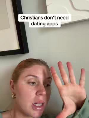 A selfie video featuring a woman speaking. She is in front of a light wall where framed art pieces can also be seen next to her.