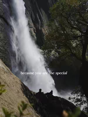 A majestic waterfall cascades down a dark rock face, the water a bright white against the somber backdrop. In the foreground, silhouetted figures sit on a rock, observing the scene. A few trees stand out on the right side and a simple text overlay reading.