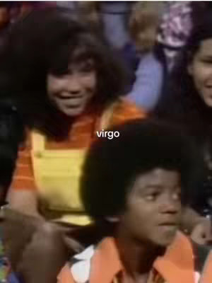 The image shows a vintage-style scene with two young people. The foreground features a young Michael Jackson, looking to the right with an expression of surprise or interest. He wears an orange collared shirt. Beside him is a young woman, smiling, and wearing an orange striped shirt under yellow overalls. The backdrop has other blurry figures suggesting a group setting, with the text 'virgo' overlaid on the image.